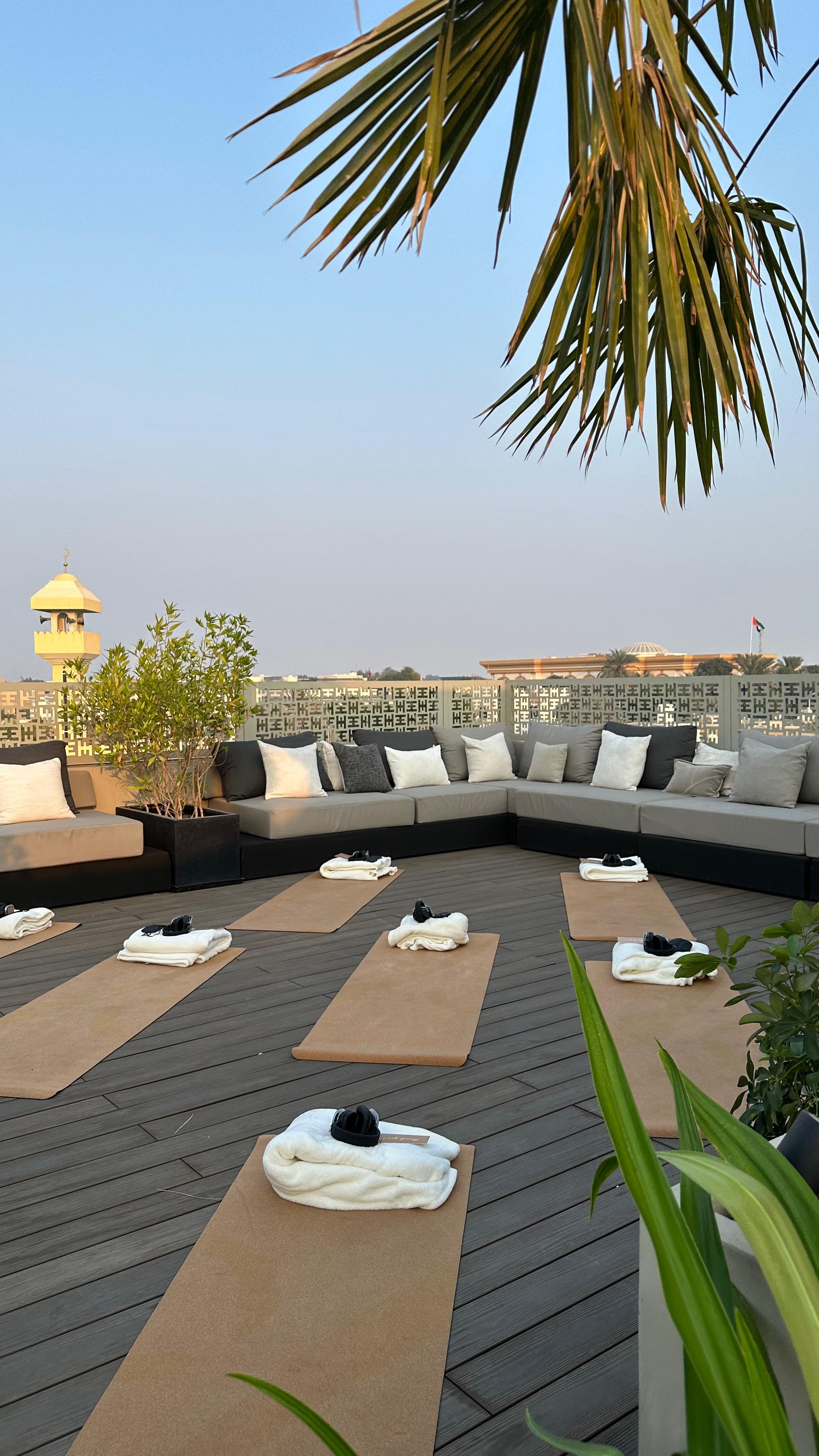 Yoga mats and accessories on the Halm wellness centre rooftop deck with palm trees, majlis seating and a Dubai cityscape view in the background.