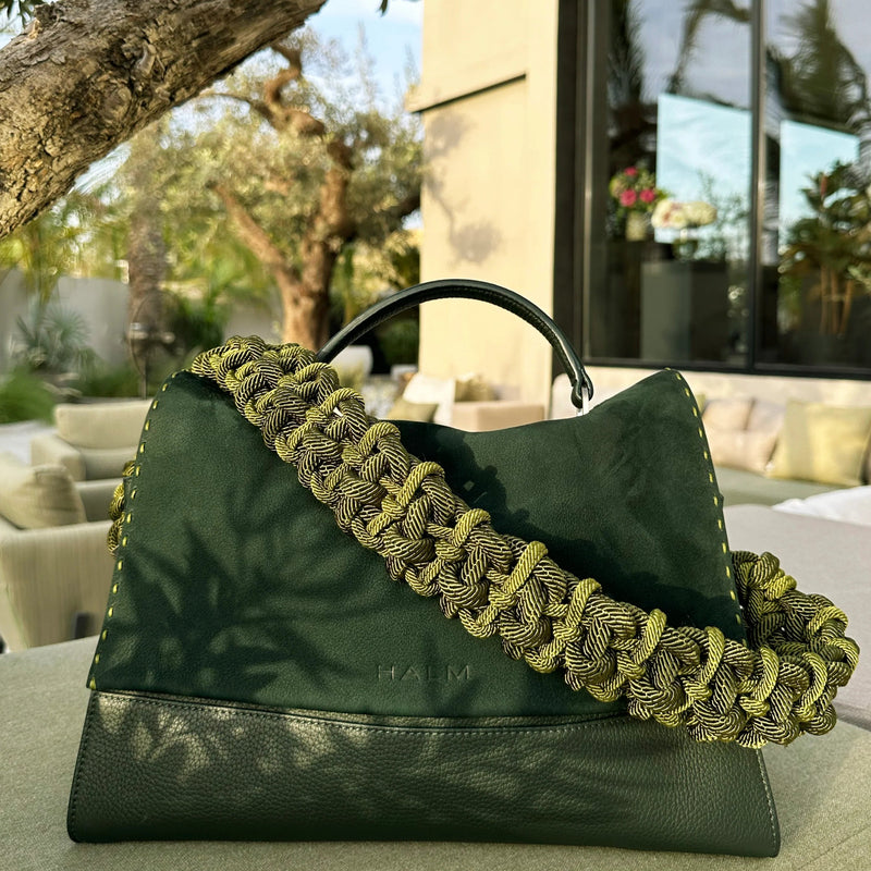 Green Halm leather handbag with thick woven rope strap, made in the UAE. Placed on a travertine table next to an olive tree. Available at Halm Collective concept store, Jumeirah beach road.