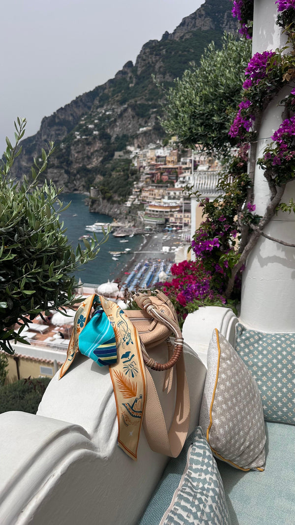 Scenic view of an Italian picturesque pastel coloured coastal town with boats and mountains, featuring a Halm luxury leather bag. Limited edition bags from Halm Collective Concept Store, Jumeirah, Dubai.