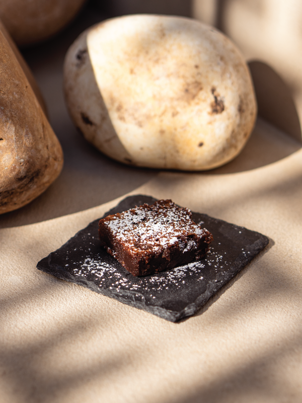 Chocolate brownie on a dark square plate with stones in the background. From the Halm Cafe menu, Jumeirah Dubai.