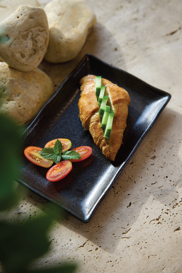 Mini croissant with whipped feta and cucumber, honey and served with tomatoes on a black dish. From the Halm Cafe menu, Jumeirah, Dubai.