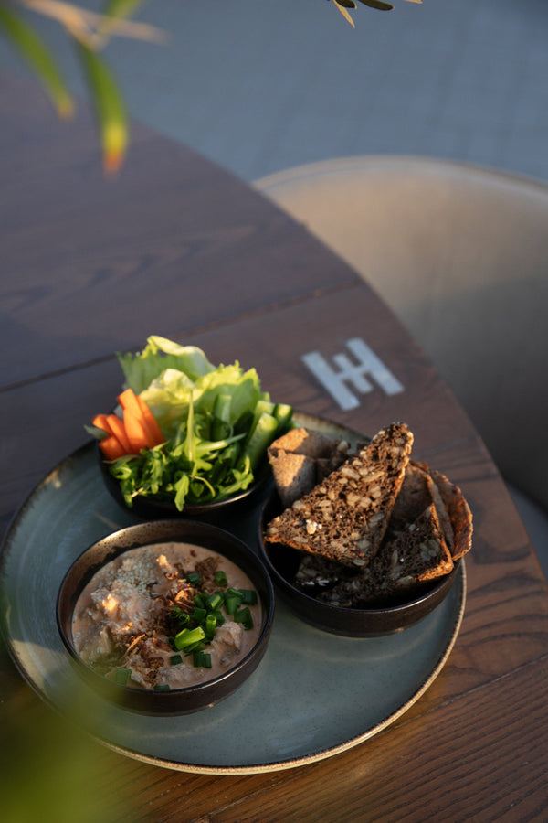 A plate of protein rich, reduced calorie dynamite chicken with a selection of salad and homemade sourdough rye bread presented on a Halm wooden table in the sunset from the Halm Cafe, 705 Jumeirah Beach Road.