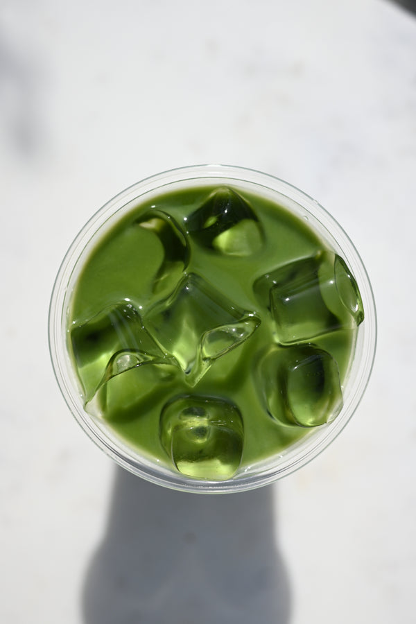 Matcha iced drink in a clear plastic cup on a white background available at Halm Cafe .