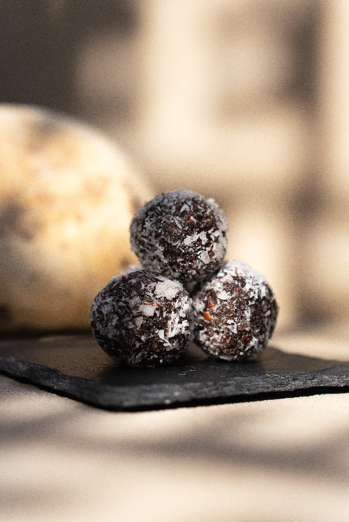 Three Swedish date chocolate balls serves on a black slate plate outside. Gluten free, UAE dates, coconut, cocoa and flax seeds. From Halm Cafe menu, Jumeirah, Dubai.