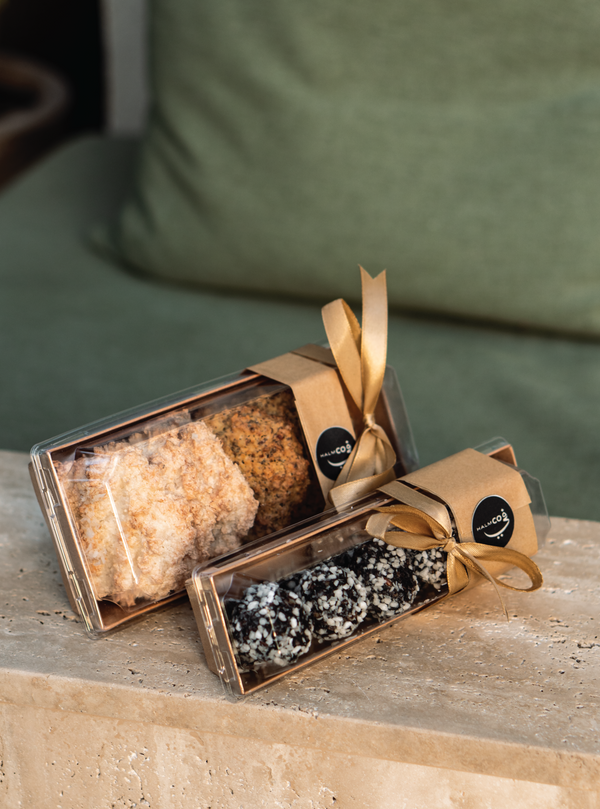 Two gift boxes with decorative ribbons on a wooden surface with a green cushioned chair in the background. Takeaway available at Halm Cafe, Jumeirah Beach Road.