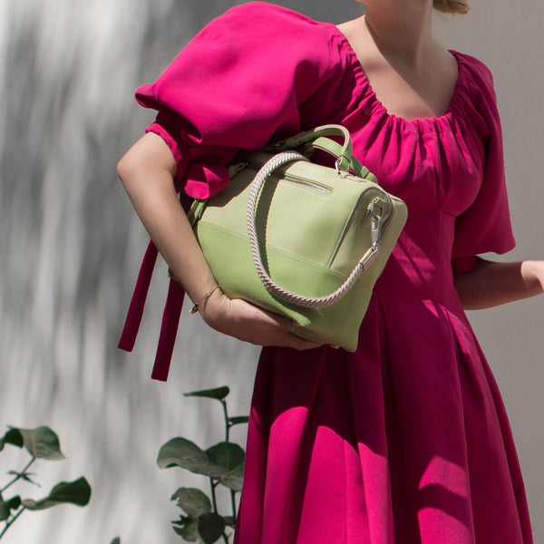 Woman in a pink dress holding a pistach green designer Halm handbag with cream strap. Available to shop at The Halm Collective Concept Store in Jumeriah.