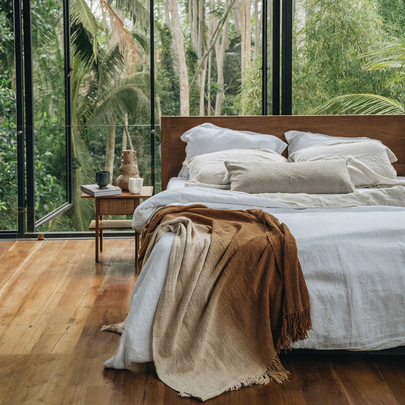Hevaya organic bamboo and linen bedding displayed in a cozy bed with wooden floor and tropical greenery. Available at Halm Collective concept store, Jumeirah beach road.