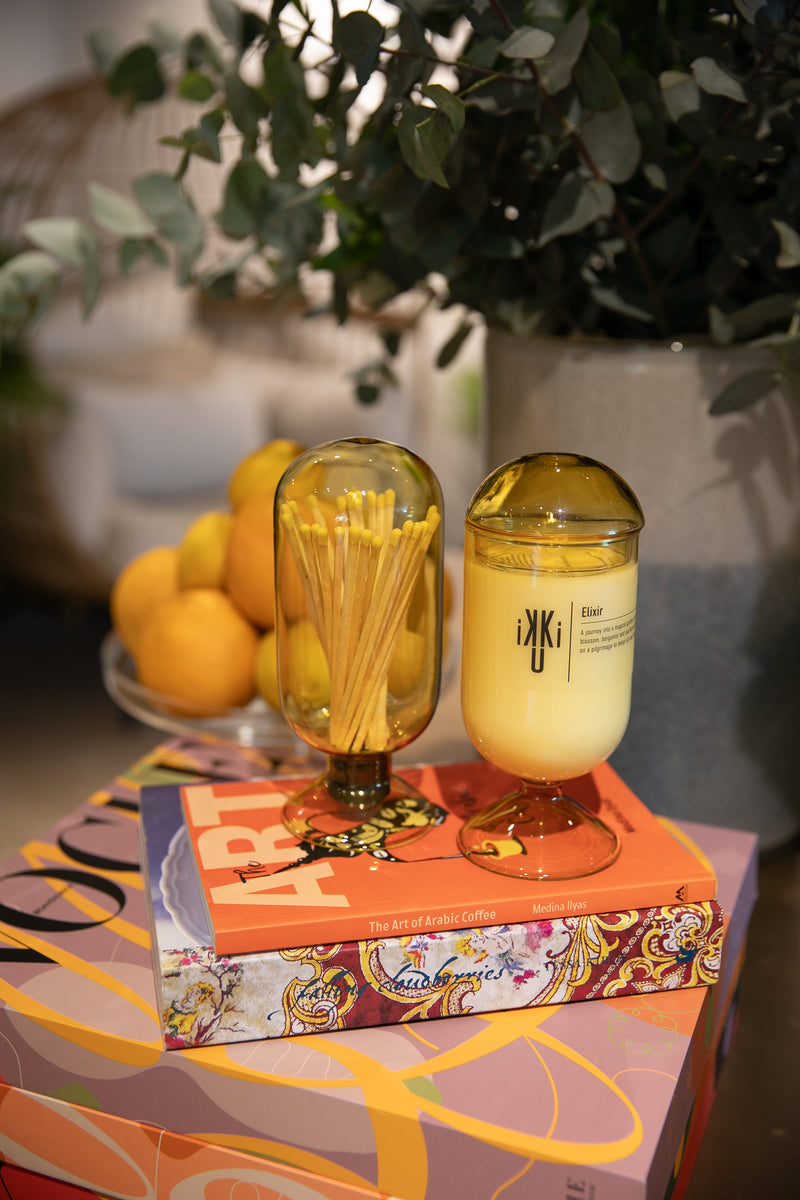 Ikku Bubbles yellow candle and matches in bubble like glass holders. Placed on decorative cooking books next to a plate of lemon and eucalyptus. Made in Dubai and available at Halm Collective concept store, Jumeirah Dubai.
