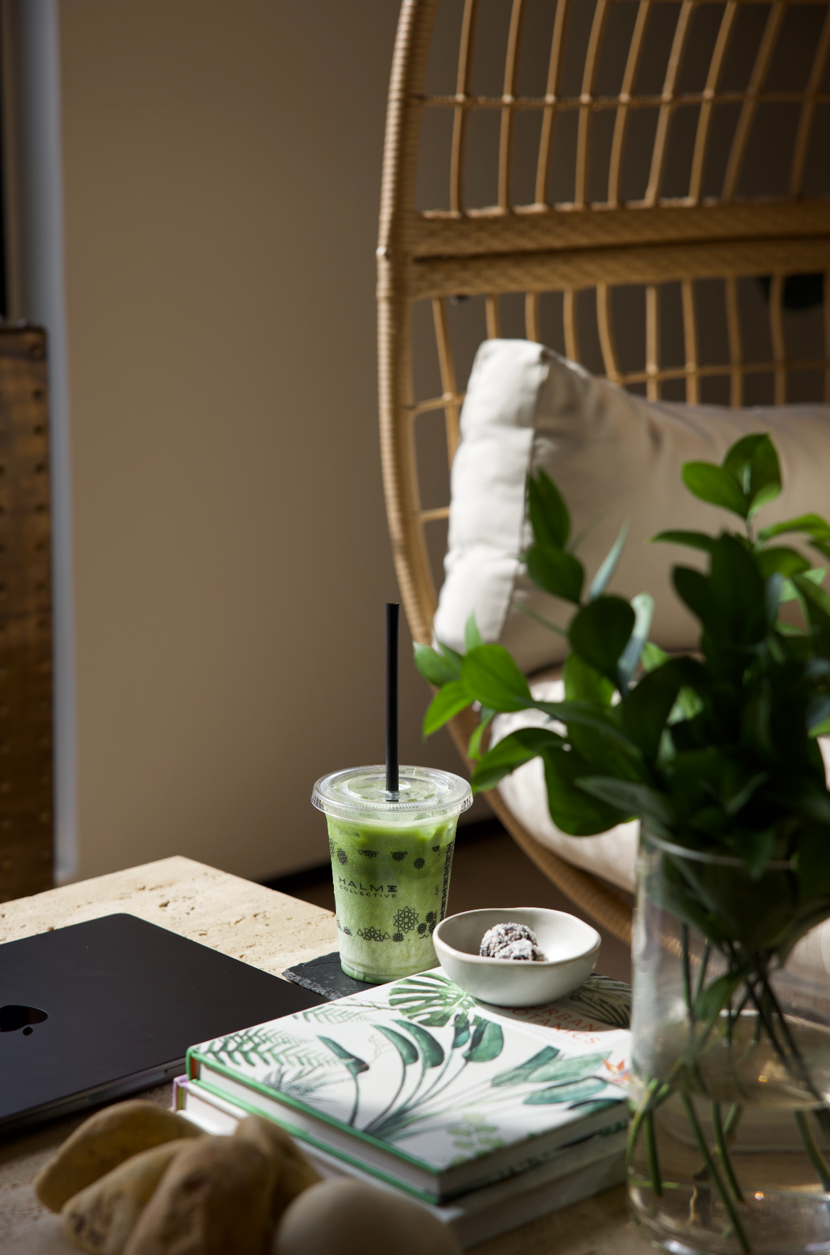 Serene moment for private or professional self focus in a quiet setting with a plush wicker chair and stylish modern setting of interesting books, greenery, organic matcha and date balls with a laptop at Halm Collective Wellness Club, Jumeirah, Dubai.