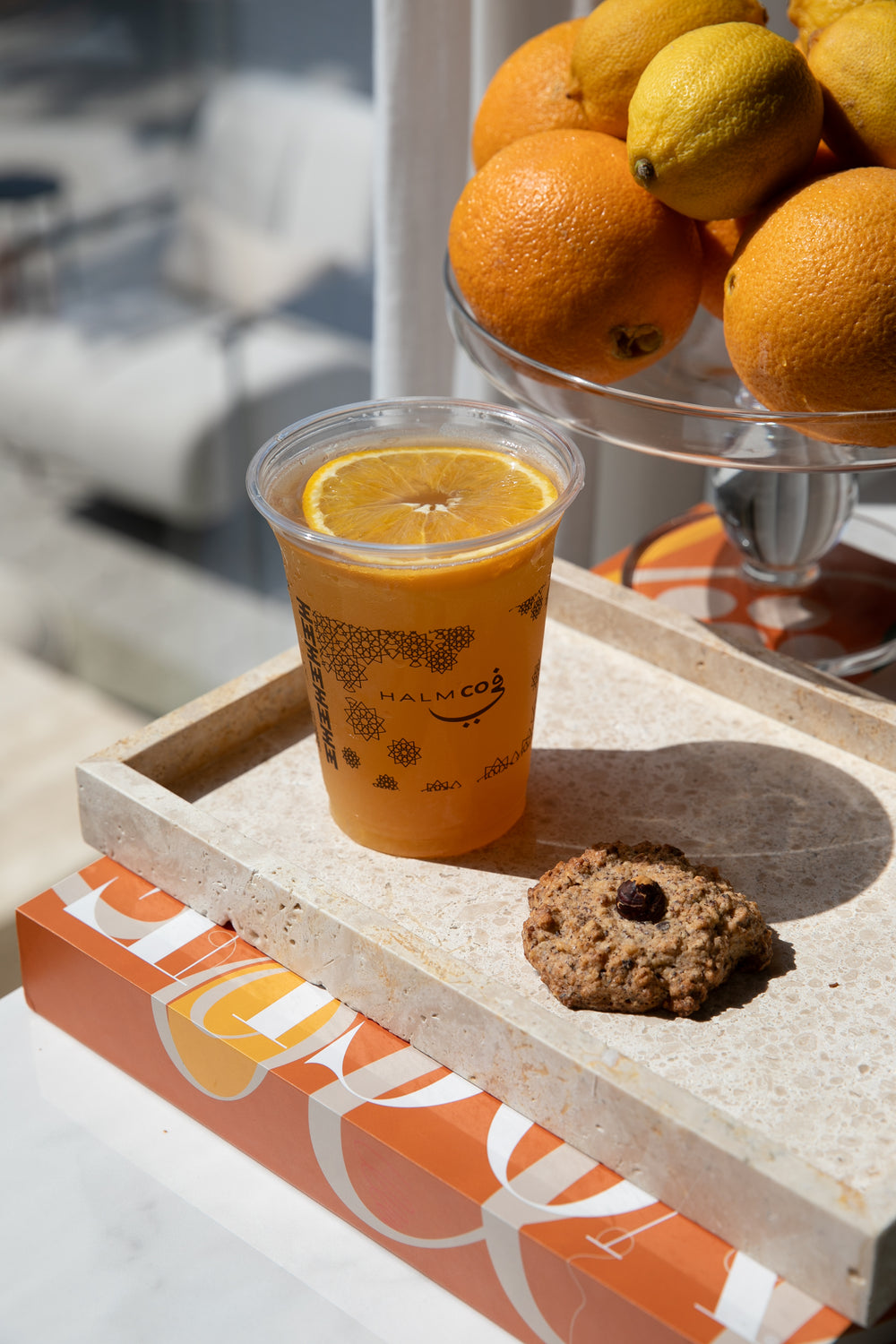 Avancha orange iced tea drink in a clear Halm cup on a marble tray with a Swedish hazelnut cookie from the Halm cafe in Umm Suqeim, Dubai. 