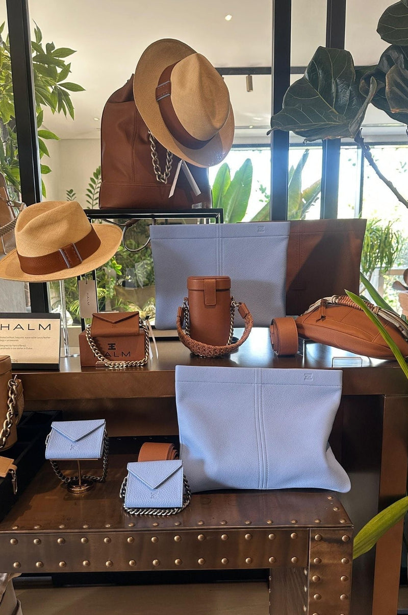 Display of hats, bags, and accessories on a wooden table with plants in the background.