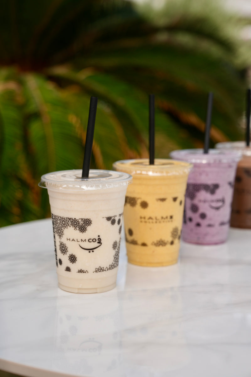 Row of protein shakes with straws on a marble surface, blurred greenery in the background. 
