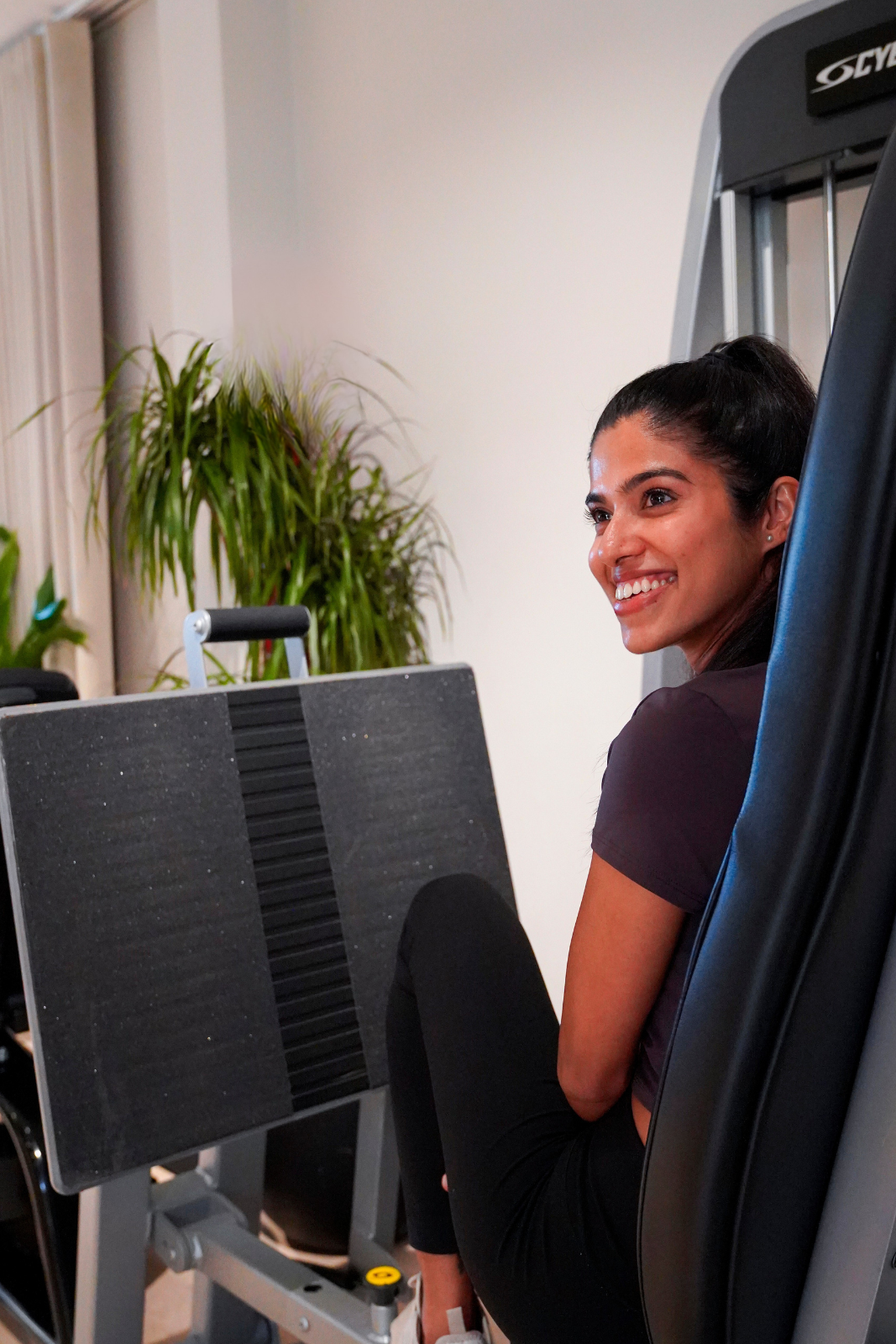 Woman smiling while using gym equipment at The Halm Collective Wellness Club in Dubai.