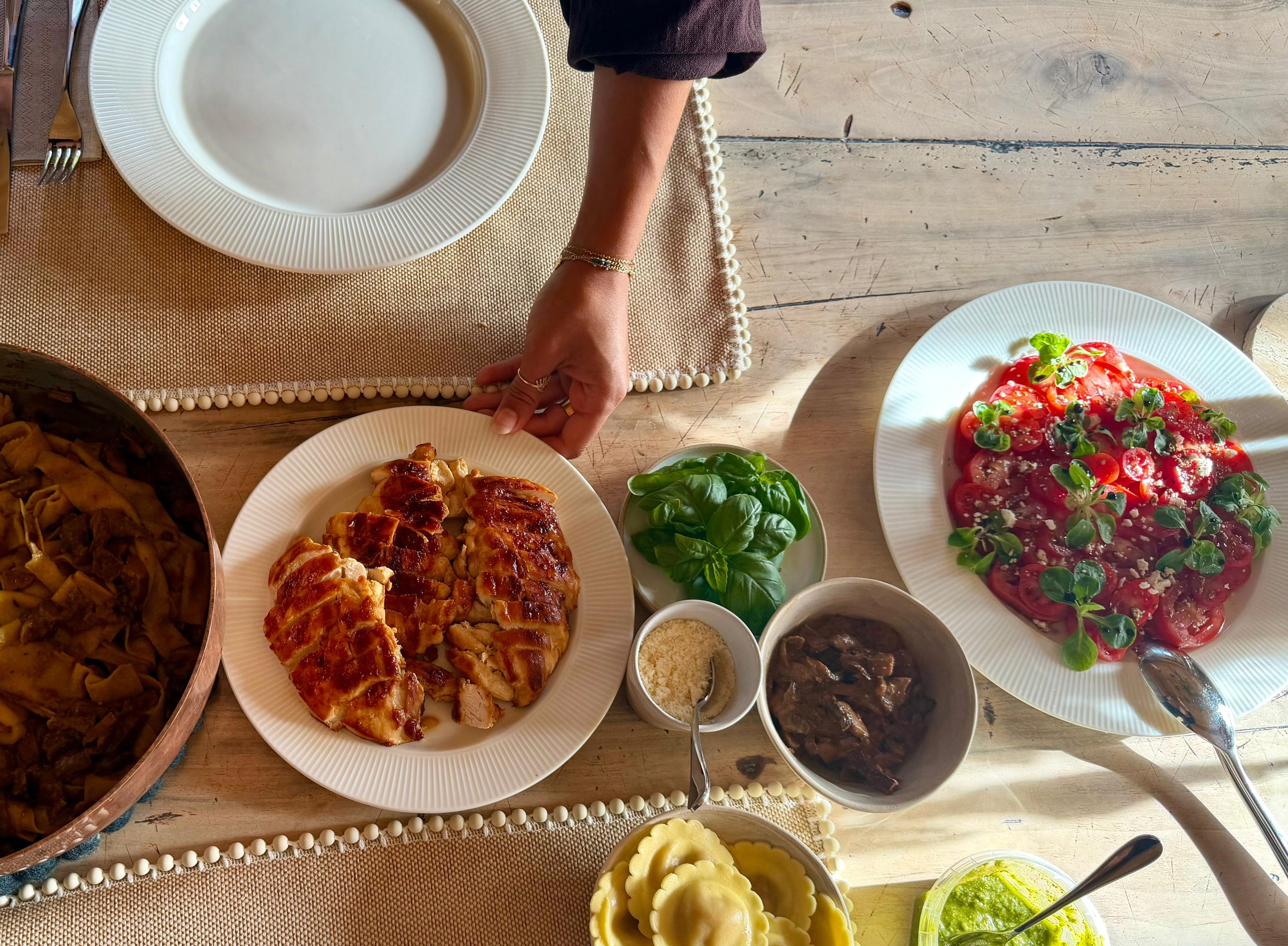 view of a fresh meal with grilled chicken, pasta, ravioli, tomato salad and basil served on a rustic dining table.