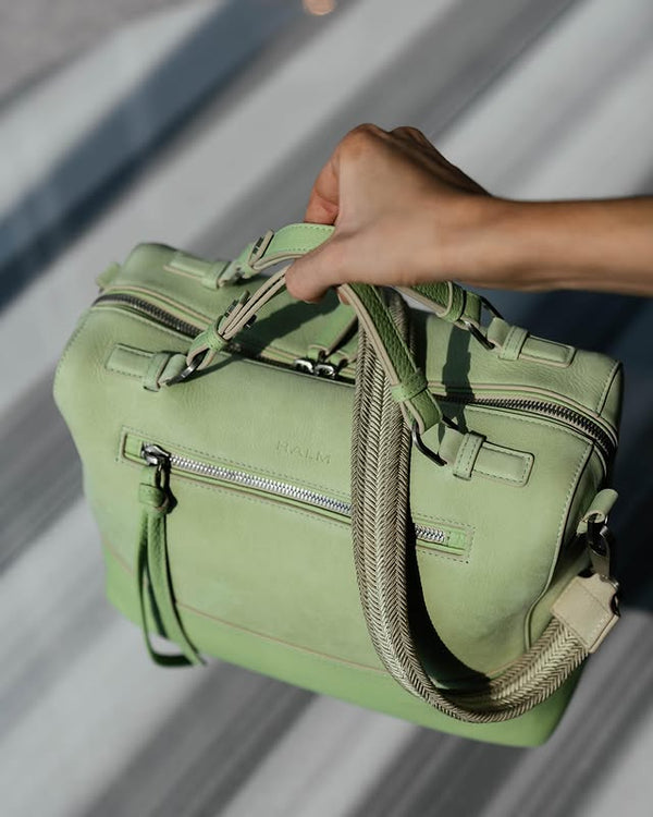 Pistach green leather and nubuck Halm handbag held by a person in a garden. Available to shop at Halm Collective curated concept store, 705 Jumeirah Beach Road. 