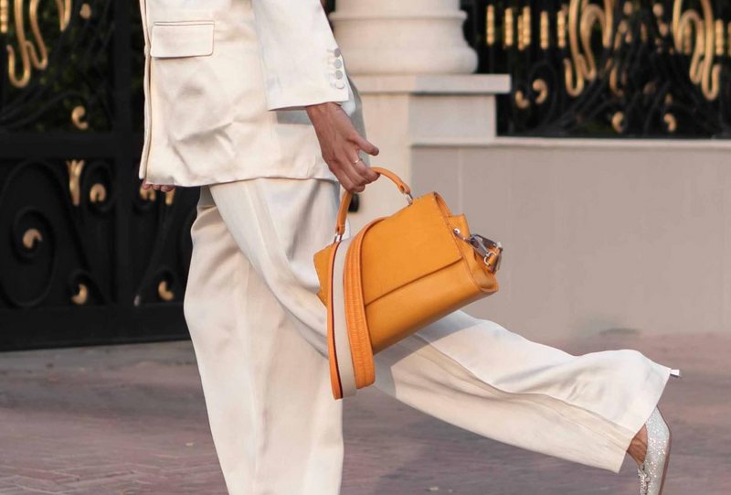 Lady wearing a white outfit with a mango coloured baby chilluxe Halm handbag, walking on a street.
