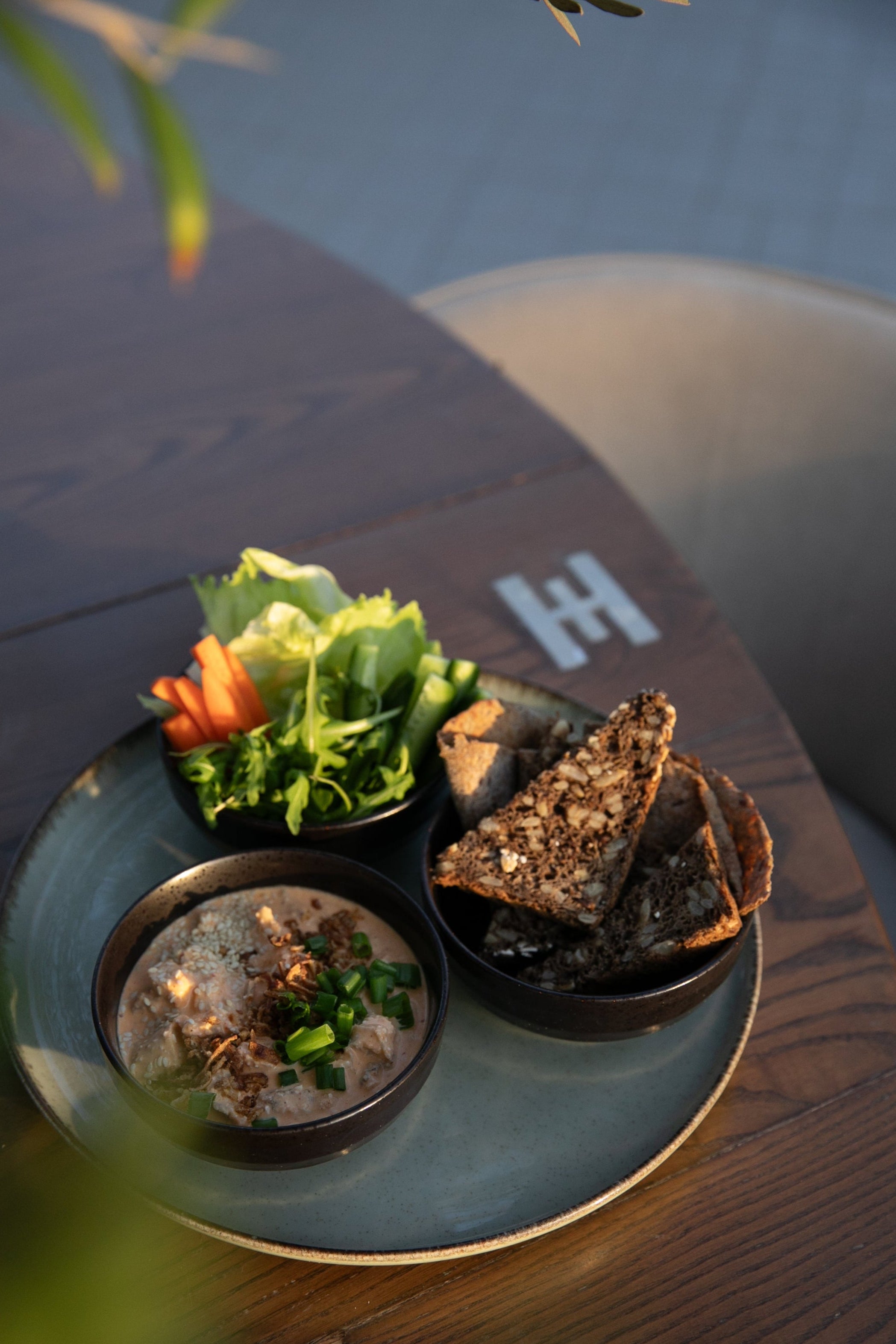 A plate of protein rich, reduced calorie dynamite chicken with a selection of salad and homemade sourdough rye bread presented on a Halm wooden table in the sunset from the Halm Cafe, 705 Jumeirah Beach Road. 