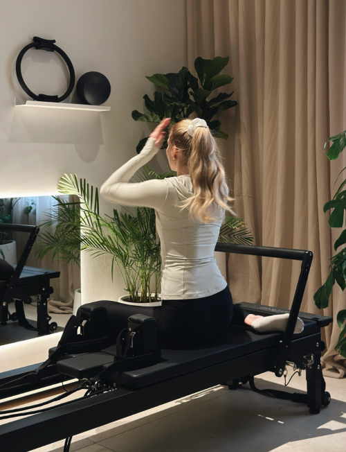 Blonde lady adjusting the pilates reformer machine in front of the mirror in green and bright private session studio in Jumeirah, Dubai. 