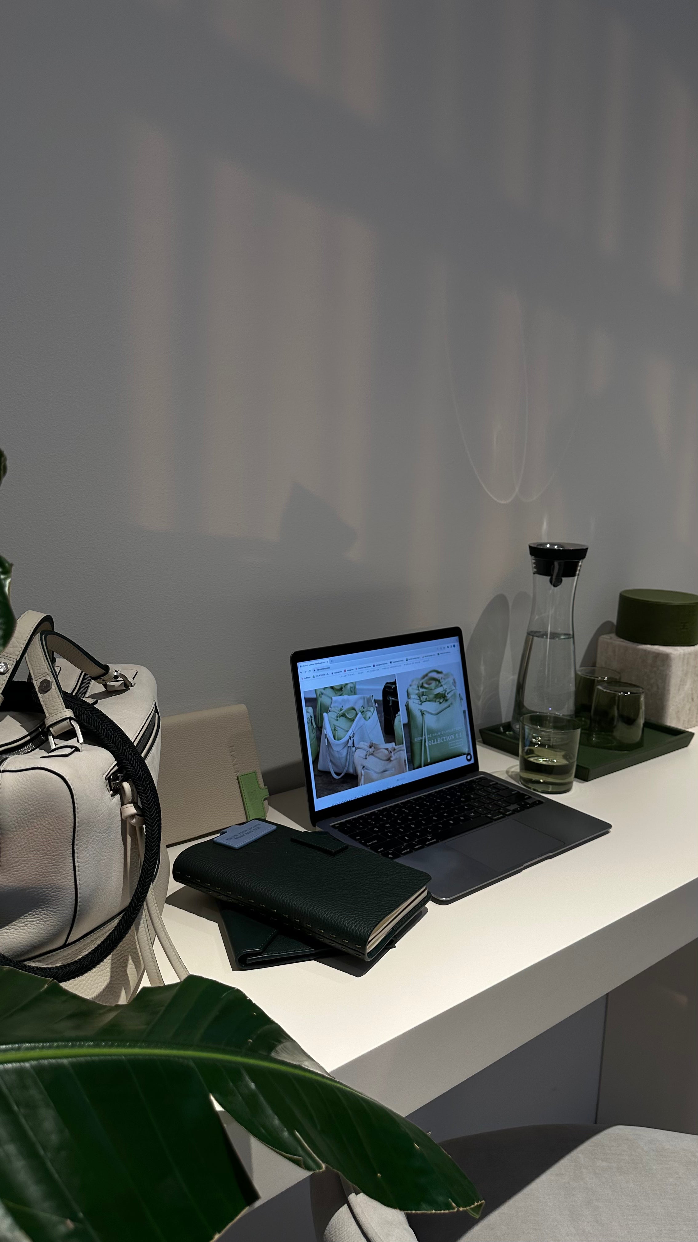 Sleek comfortable work desk setup corner 
with a laptop displaying a website, a glass of detox water, a cream limited edition Halm bag, creating a calm and organised meeting space, Jumeirah, Dubai. 